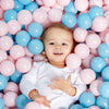 Enfant souriant allongé dans un océan de balles à piscine roses et bleues