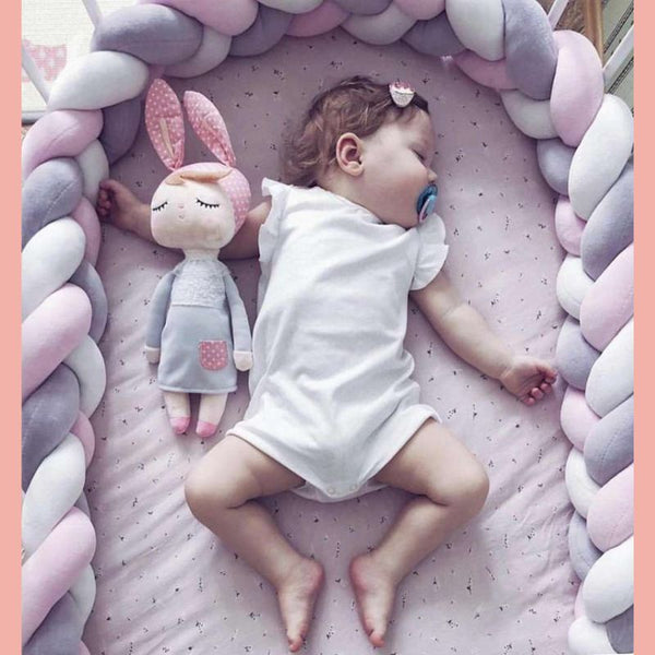 un bébé dormant dans son berceau avec une tresse de lit bébé blanc-gris-rose autour de lui