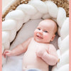 Un bébé souriant allongé dans son berceau avec une tresse de lit bébé blanche autour de lui