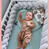 Un bébé allongé dans son berceau avec une tresse de lit bébé grise autour de lui