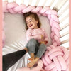 Une petite fille riant dans son berceau avec une tresse de lit bébé rose autour d'elle