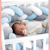 Un bébé dormant dans son berceau avec une tresse de lit bébé blanc-gris-bleu autour de lui